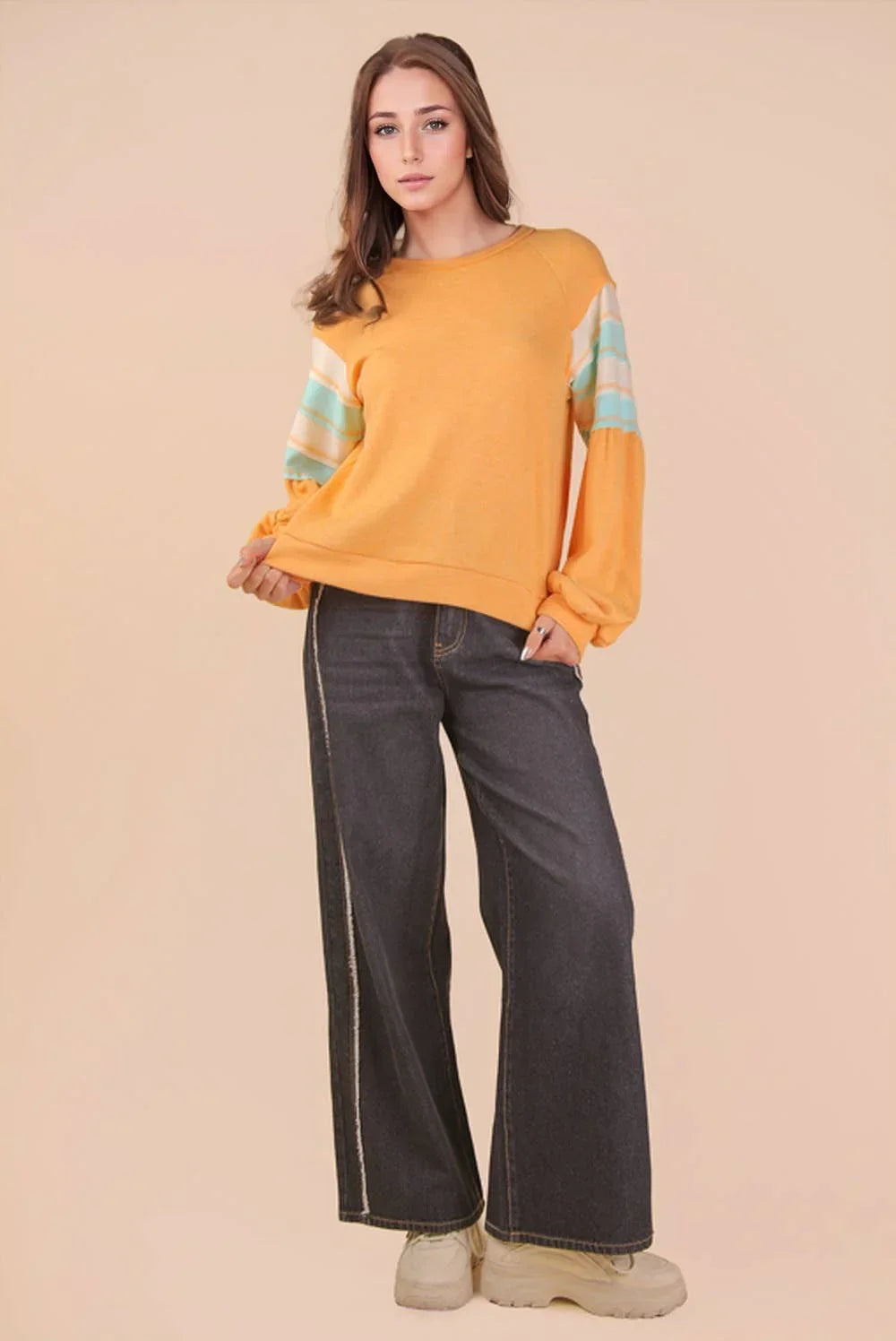Woman modeling yellow sweater with striped sleeves and wide leg dark denim jeans
