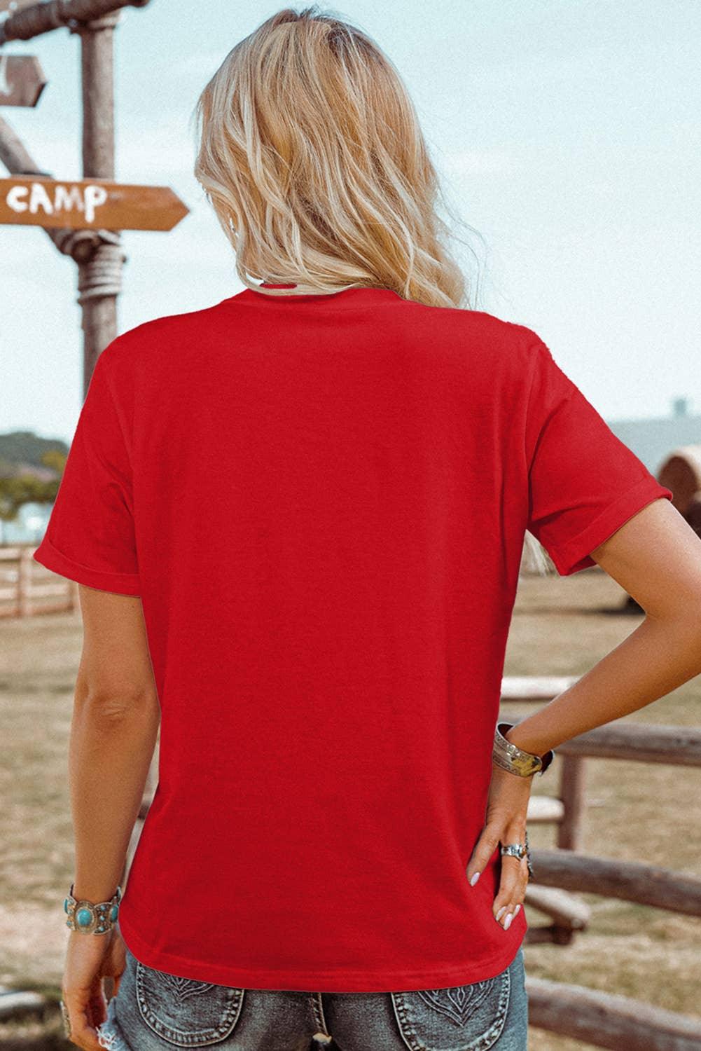 Red t-shirt worn by woman with blonde hair, standing near wooden 'CAMP' sign, paired with denim shorts