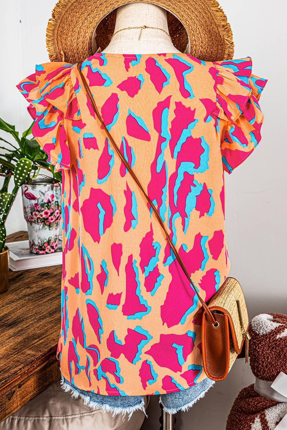 Vibrant pink and blue patterned blouse with ruffled sleeves, paired with denim shorts and a straw hat.
