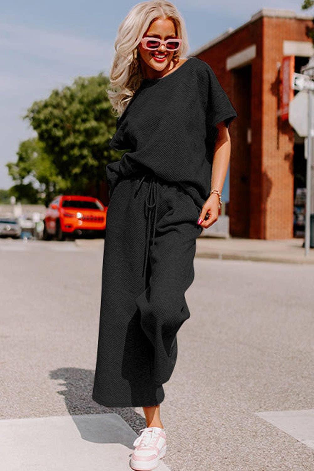 Woman in black casual matching set, pink sunglasses, and sneakers walking on city street
