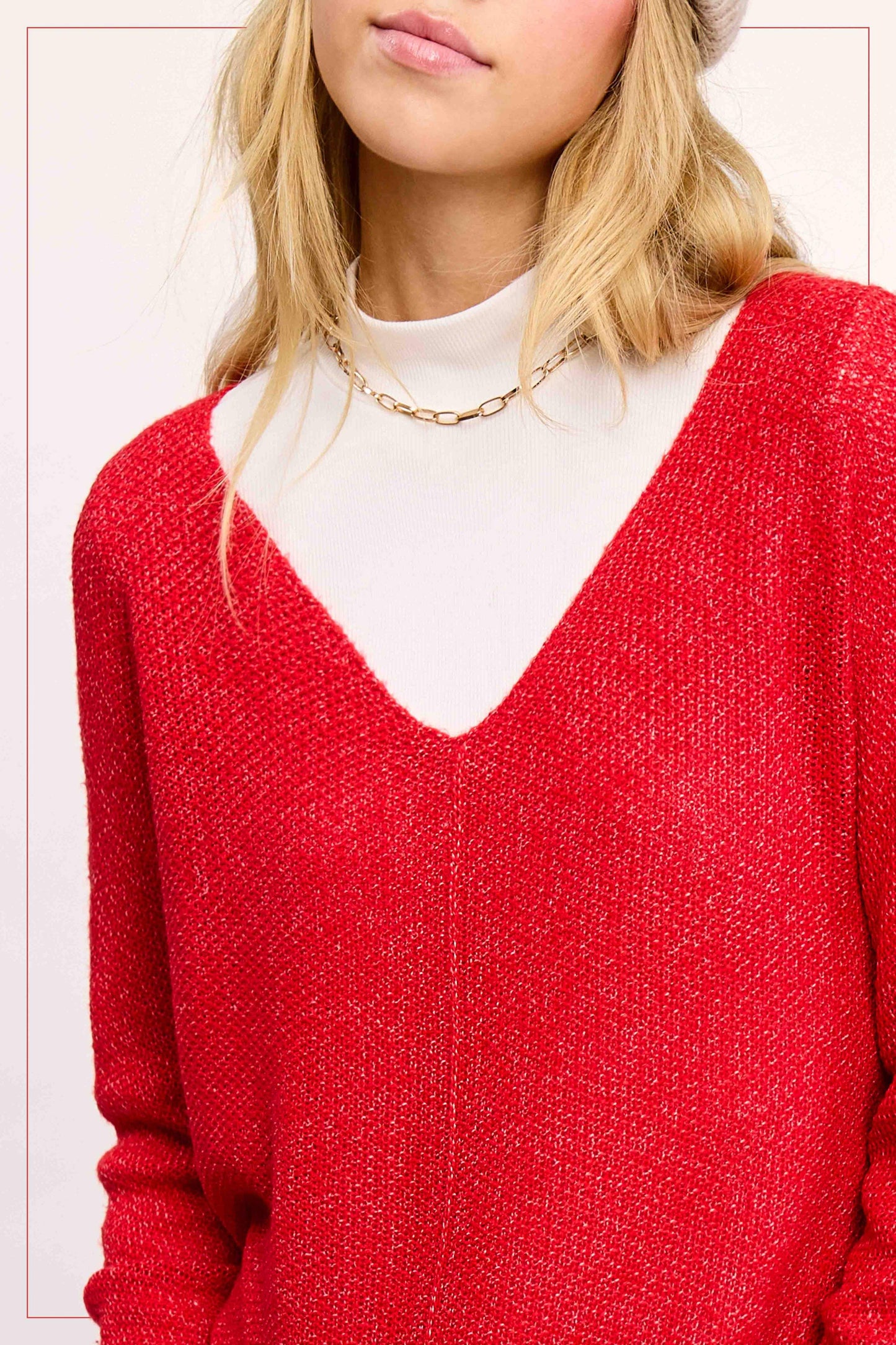 Woman wearing a textured red V-neck sweater over a white turtleneck with gold chain necklace