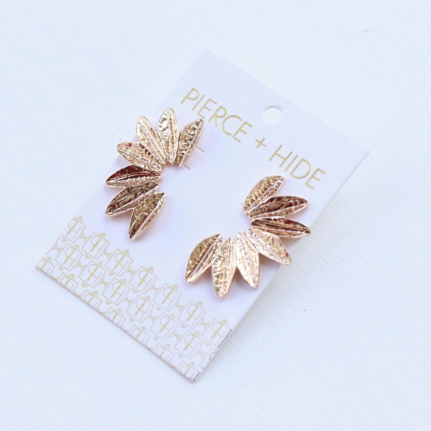 Gold leaf-shaped textured stud earrings displayed on a white card