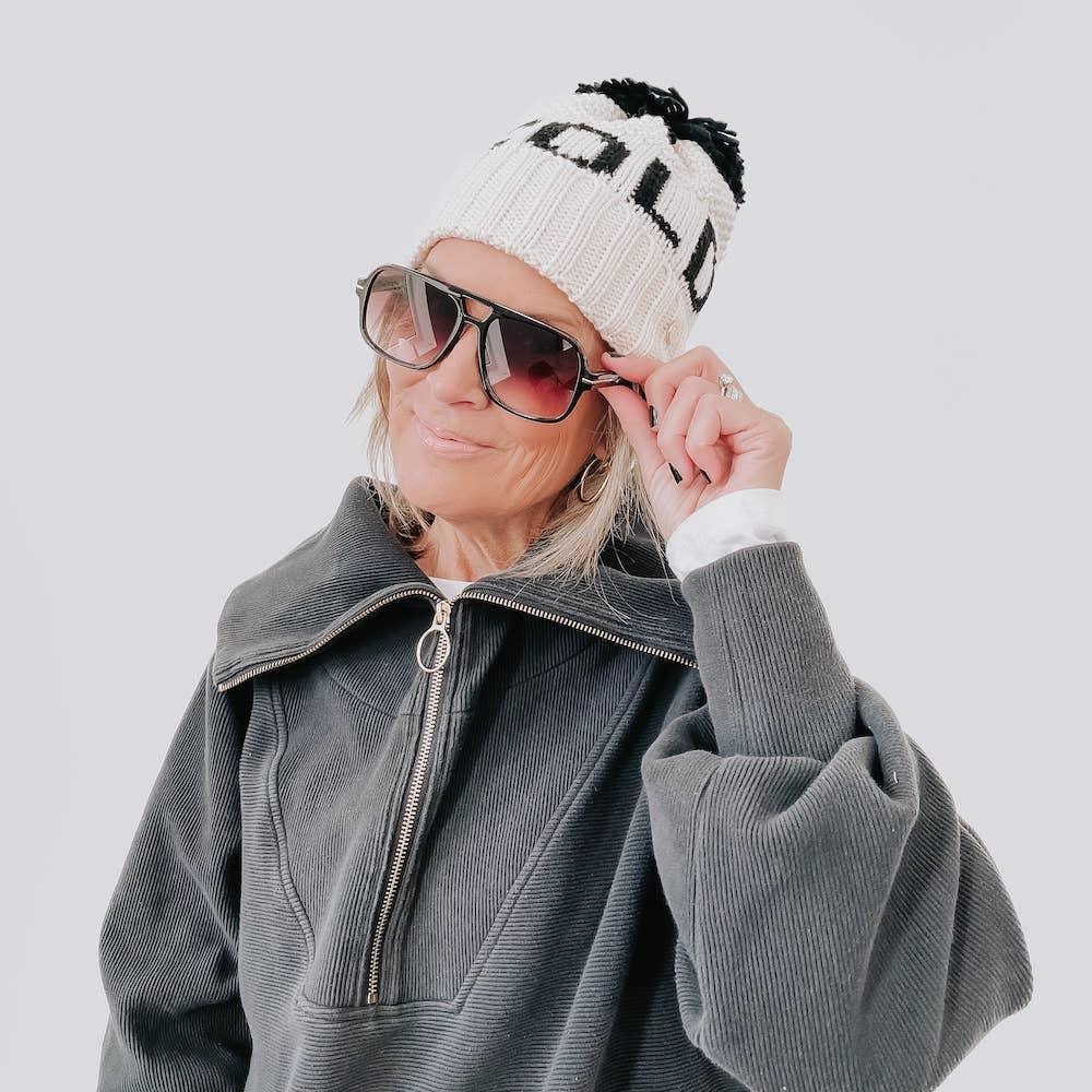 Stylish woman wearing cozy knit beanie, oversized sunglasses, and gray corduroy jacket for chic winter fashion.