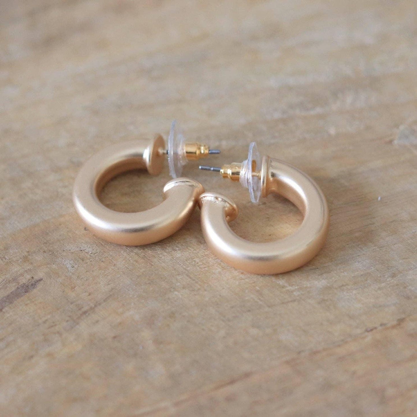 Gold chunky hoop earrings with clear backings on light wood surface