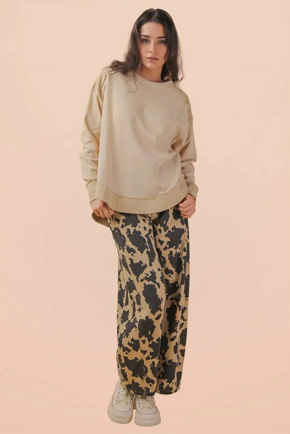 Woman in beige oversized sweatshirt and wide-leg black and tan print pants with sneakers
