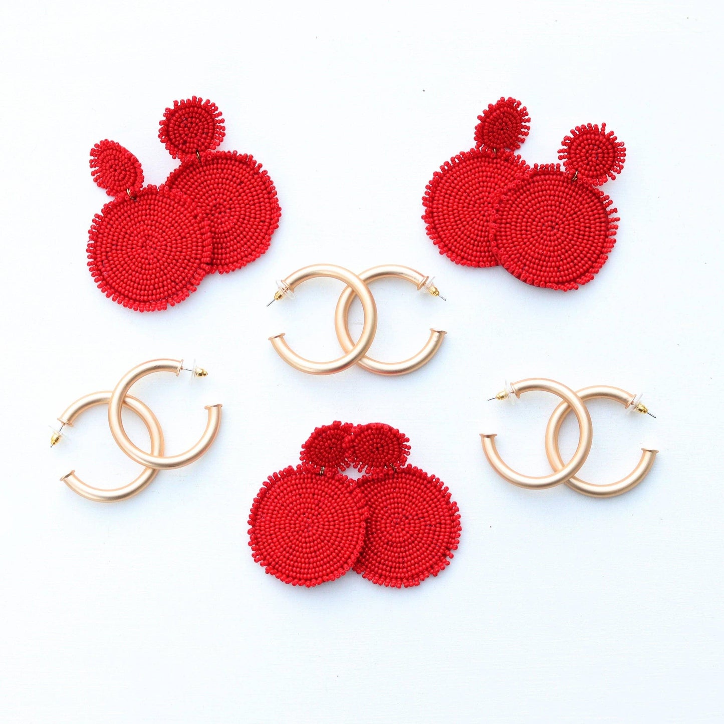 Red beaded statement earrings and gold hoop earrings arranged on a white background