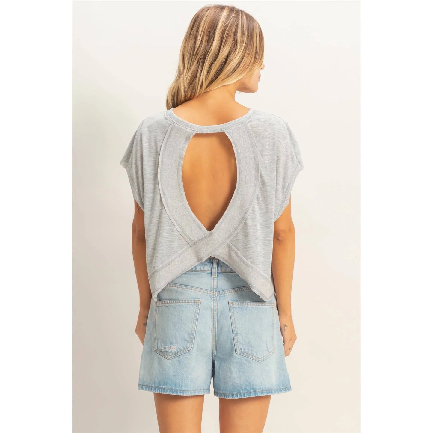 Woman wearing light gray open-back top with short sleeves and high-waist denim shorts