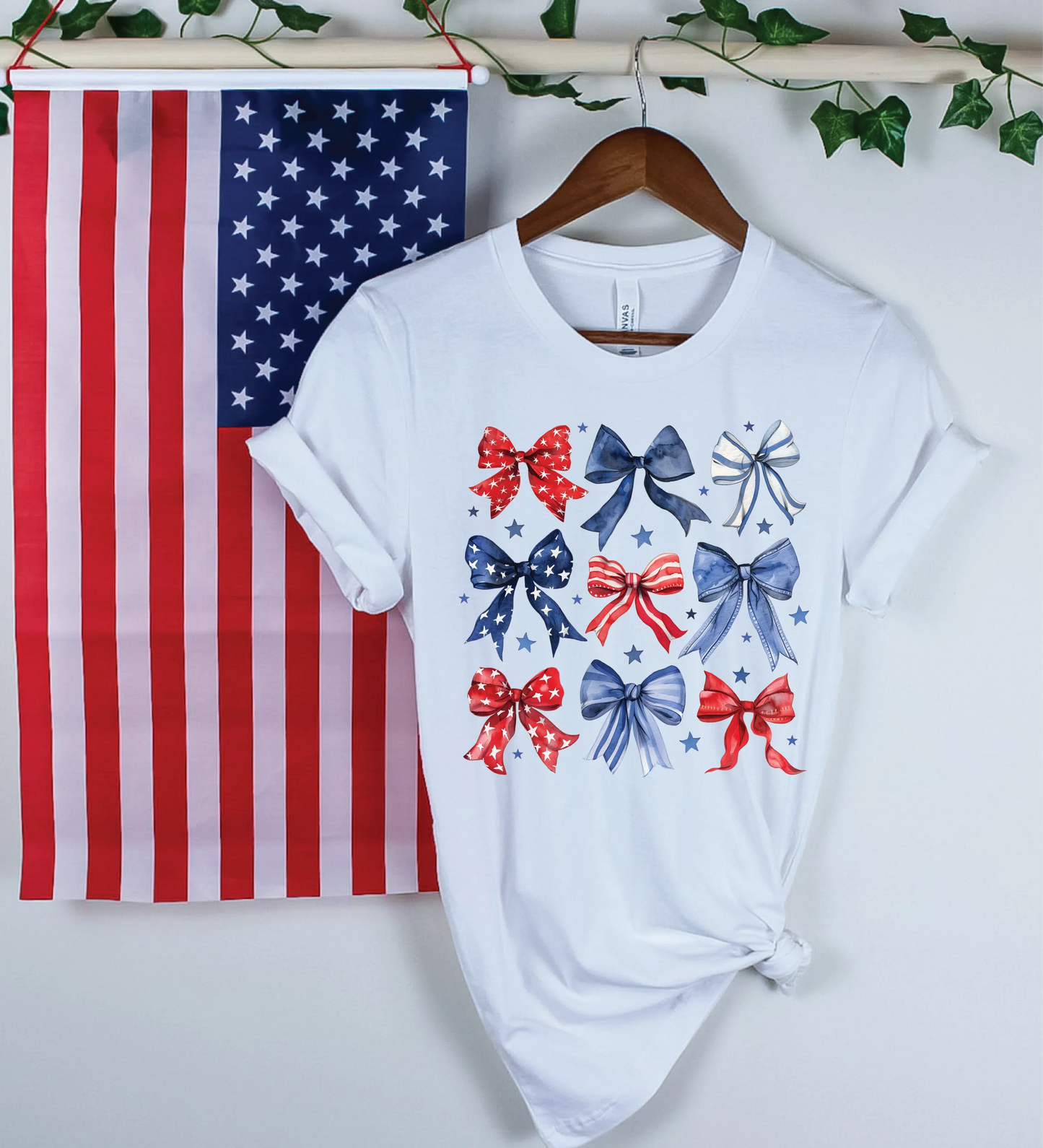 White patriotic t-shirt with red, white, and blue bow print, displayed beside American flag for 4th of July fashion.
