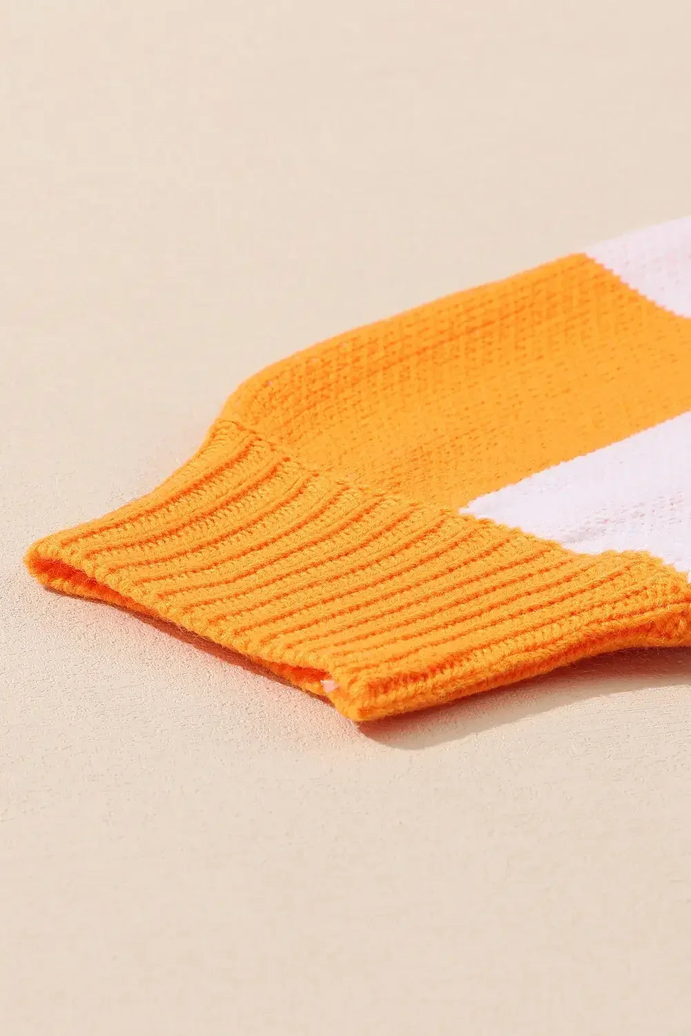 Close-up of orange and white striped knit sweater sleeve on beige background