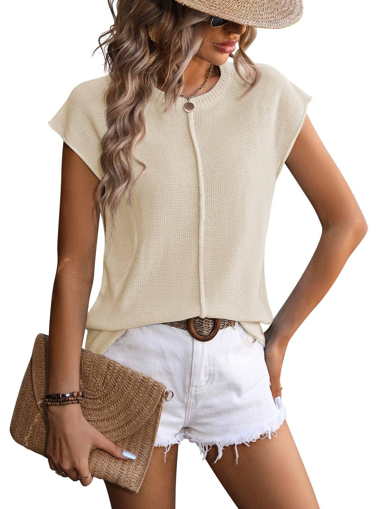 Woman wearing beige knit top, white denim shorts, straw hat, and holding woven clutch
