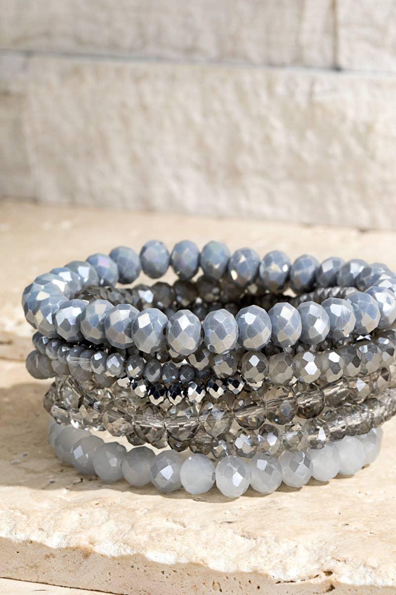 Stack of gray and silver faceted bead stretch bracelets on stone background