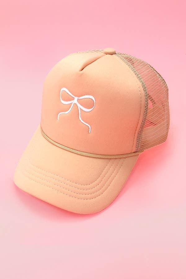 Peach mesh trucker hat with white embroidered bow on pink background
