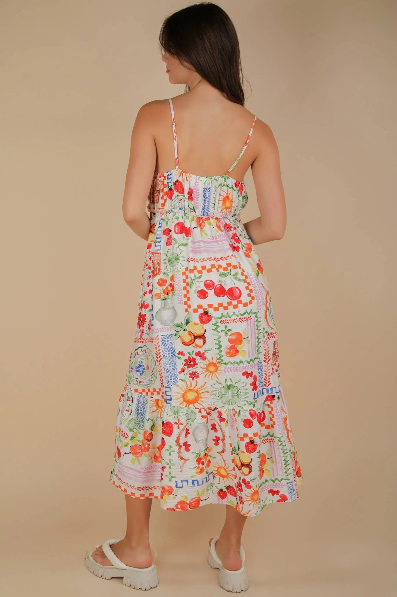 Colorful fruit-patterned midi dress with thin straps and tiered skirt, paired with white sandals.