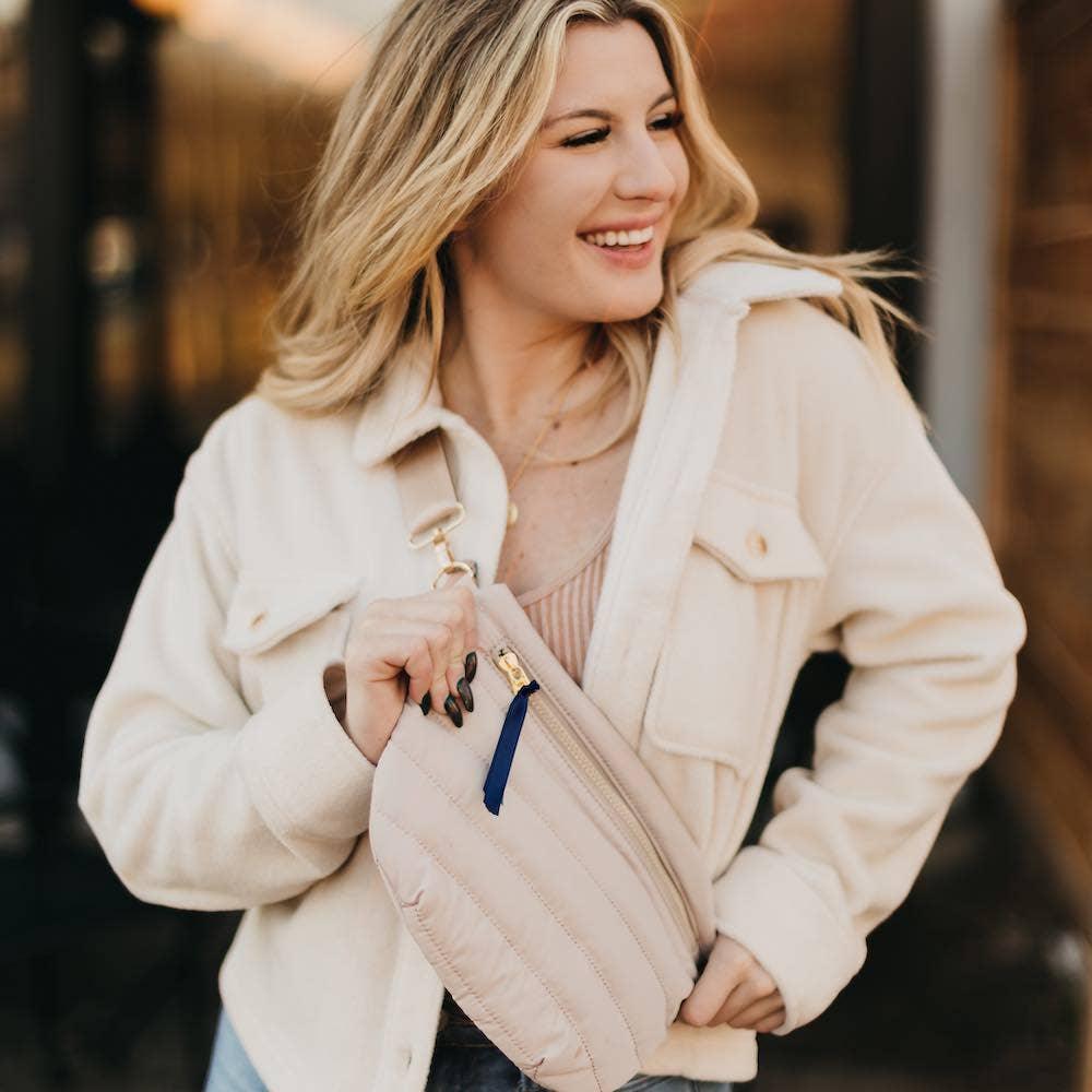 Woman in cream jacket holding quilted crossbody bag with blue zipper pull