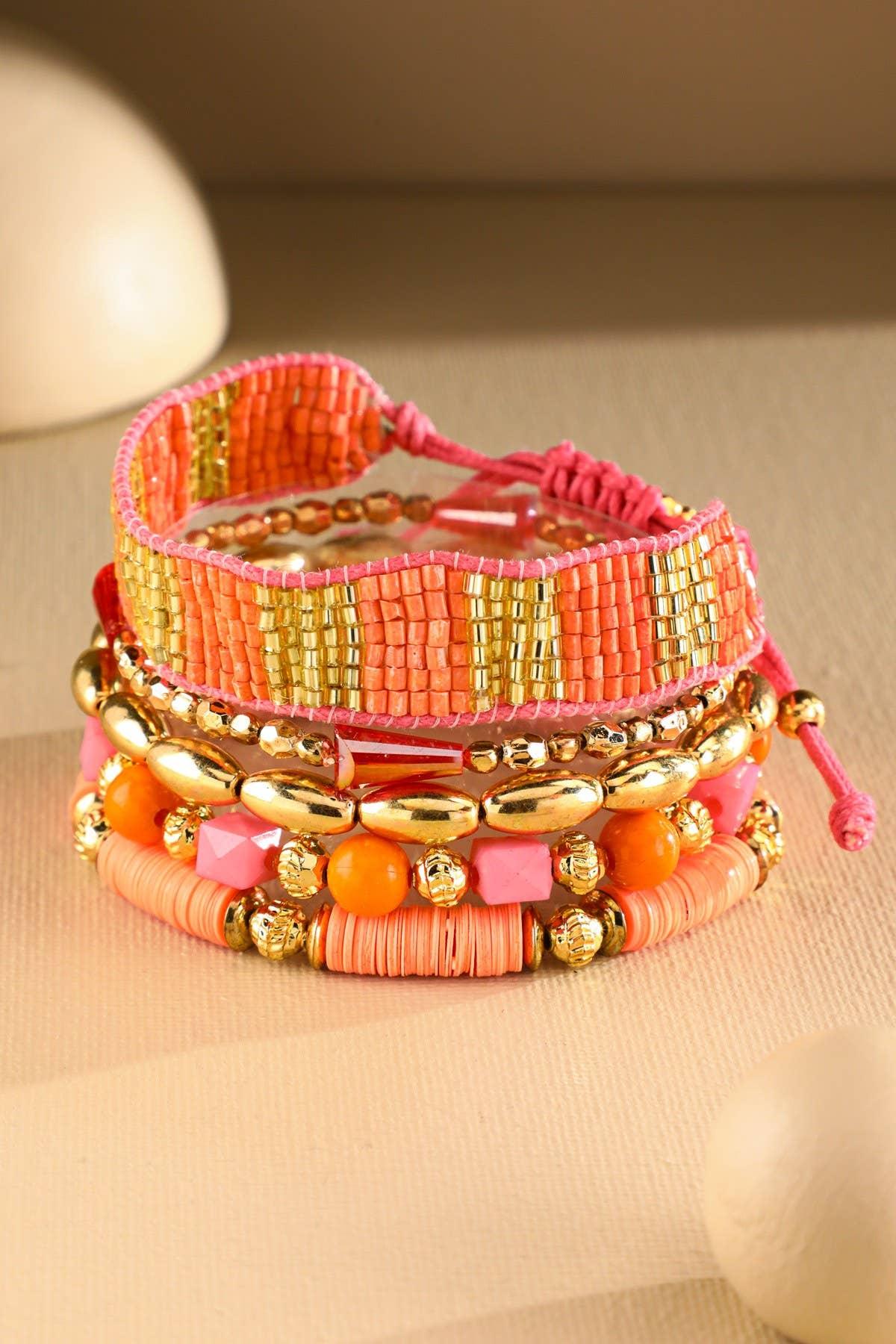 Stacked beaded bracelets in gold, orange, and pink tones on neutral background