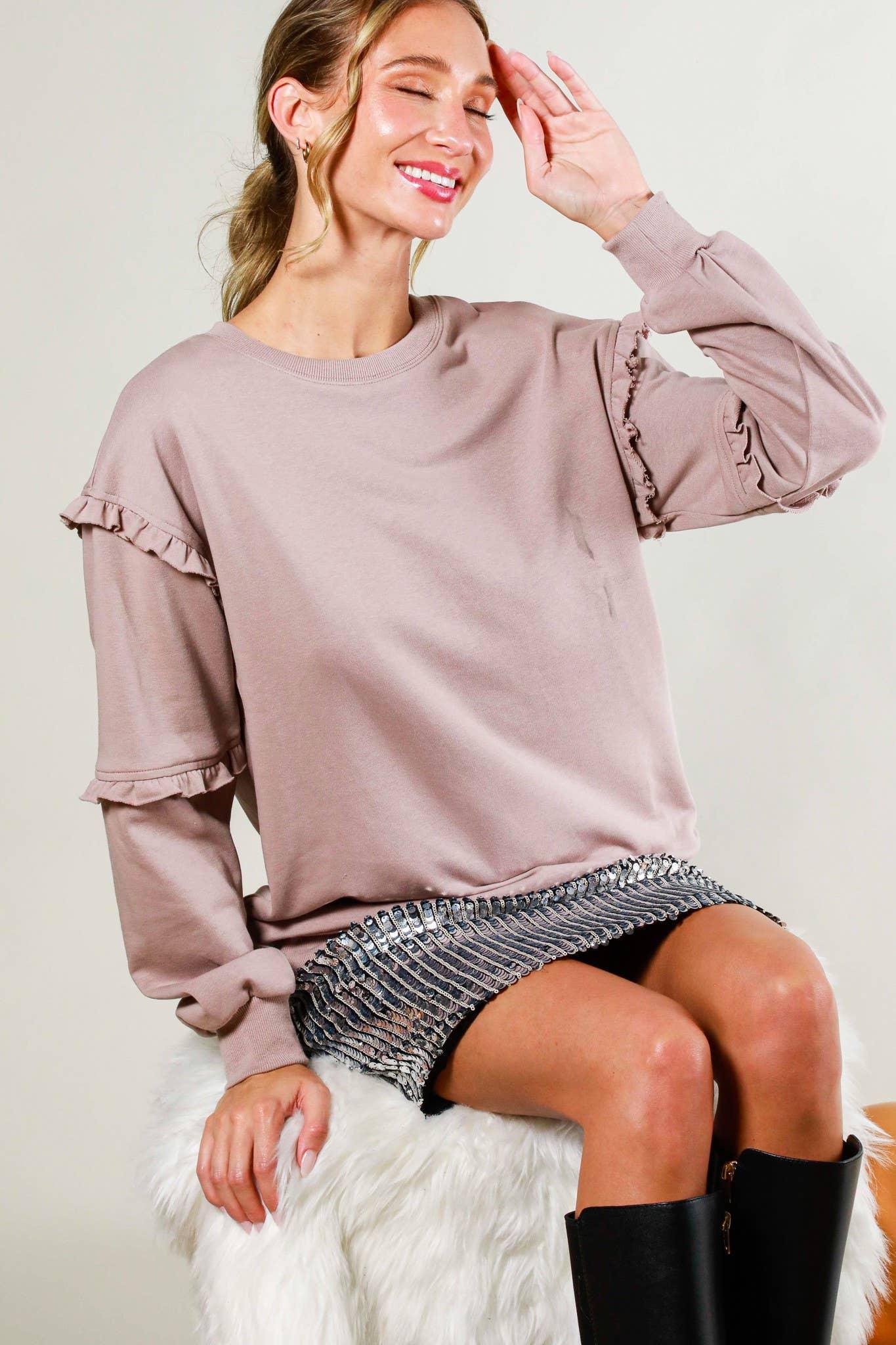 Woman wearing mauve ruffle sweatshirt with metallic mini skirt and black boots, sitting on faux fur stool