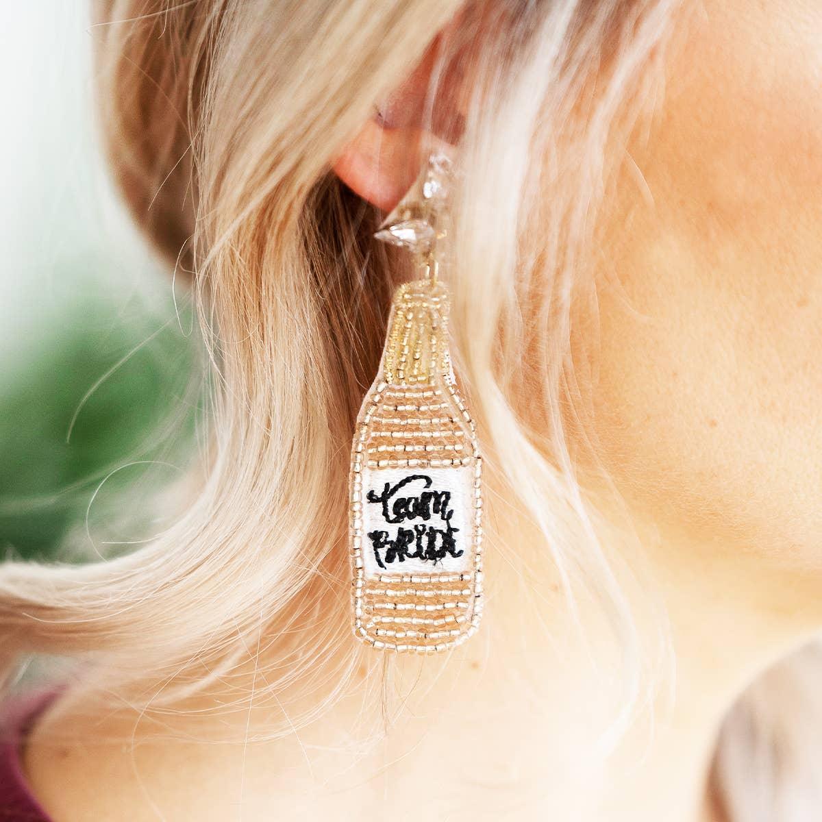 Team Bride beaded bottle earring, gold and white, worn by blonde woman