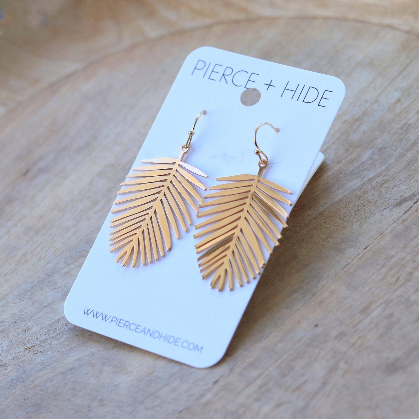 Gold palm leaf drop earrings on display card, jewelry on wooden surface