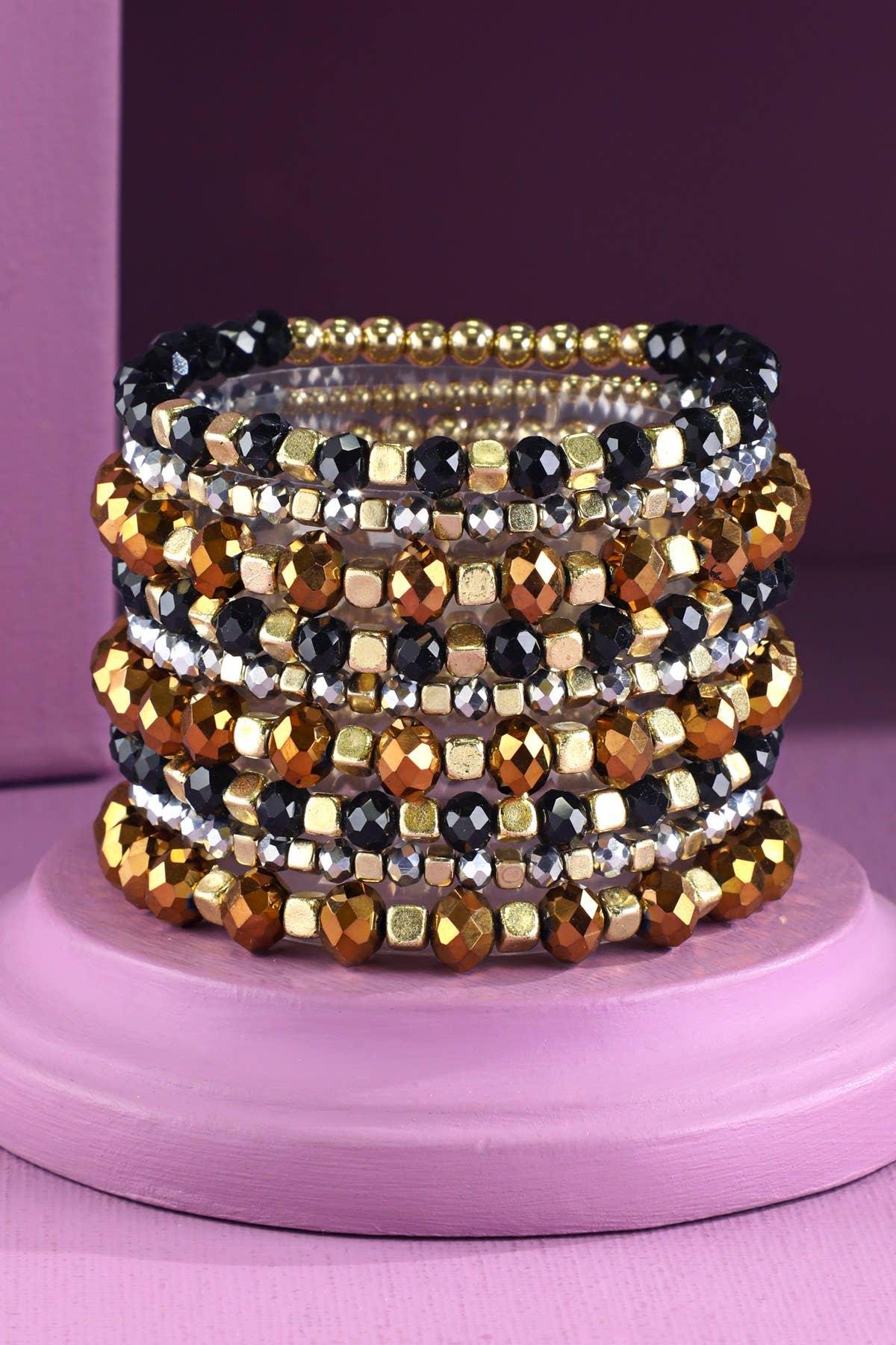 Stacked beaded stretch bracelets with gold, black, bronze, and silver faceted beads on a pink stand