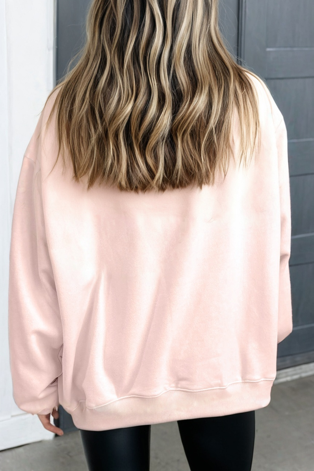 Woman wearing oversized light pink sweatshirt and black leggings, back view
