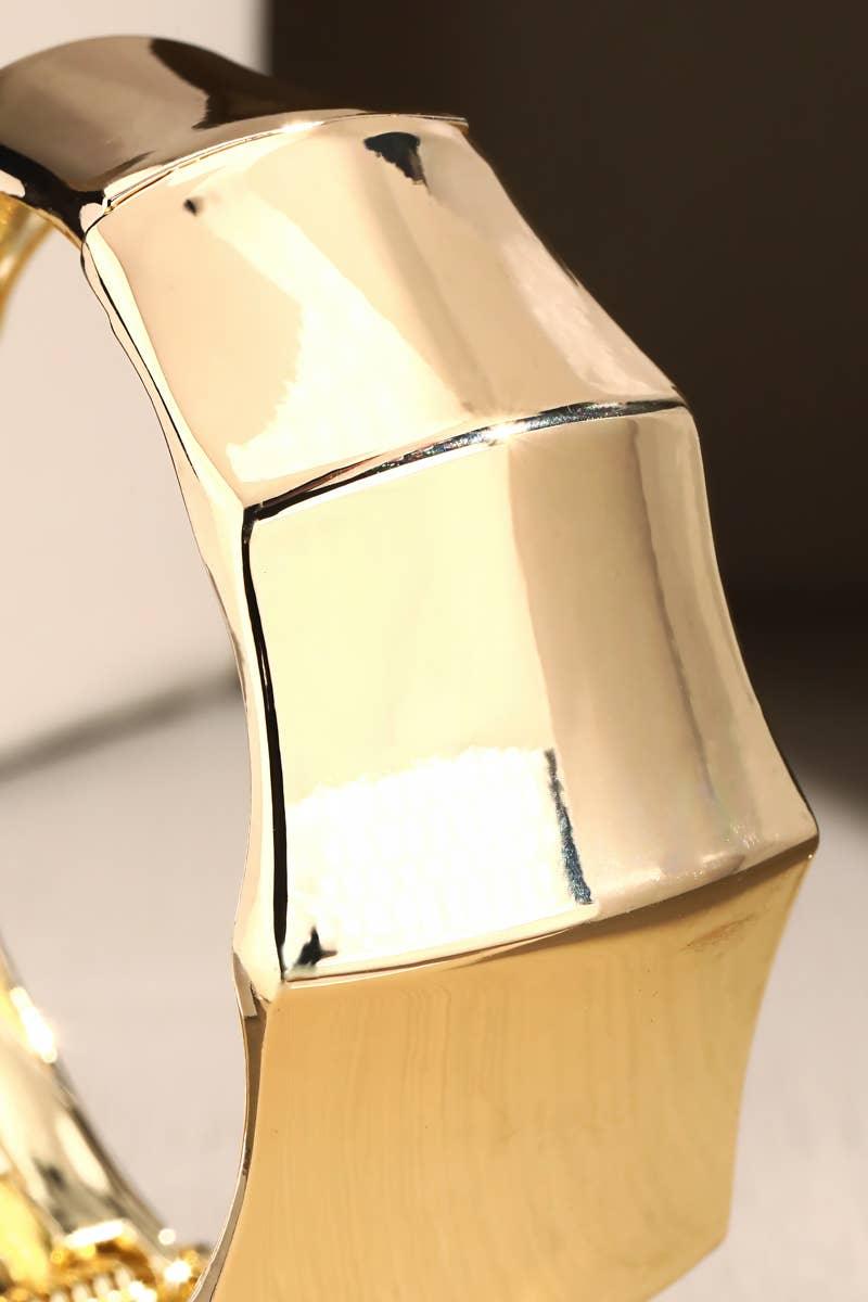 Close-up of chunky gold bangle bracelet with geometric design and polished finish