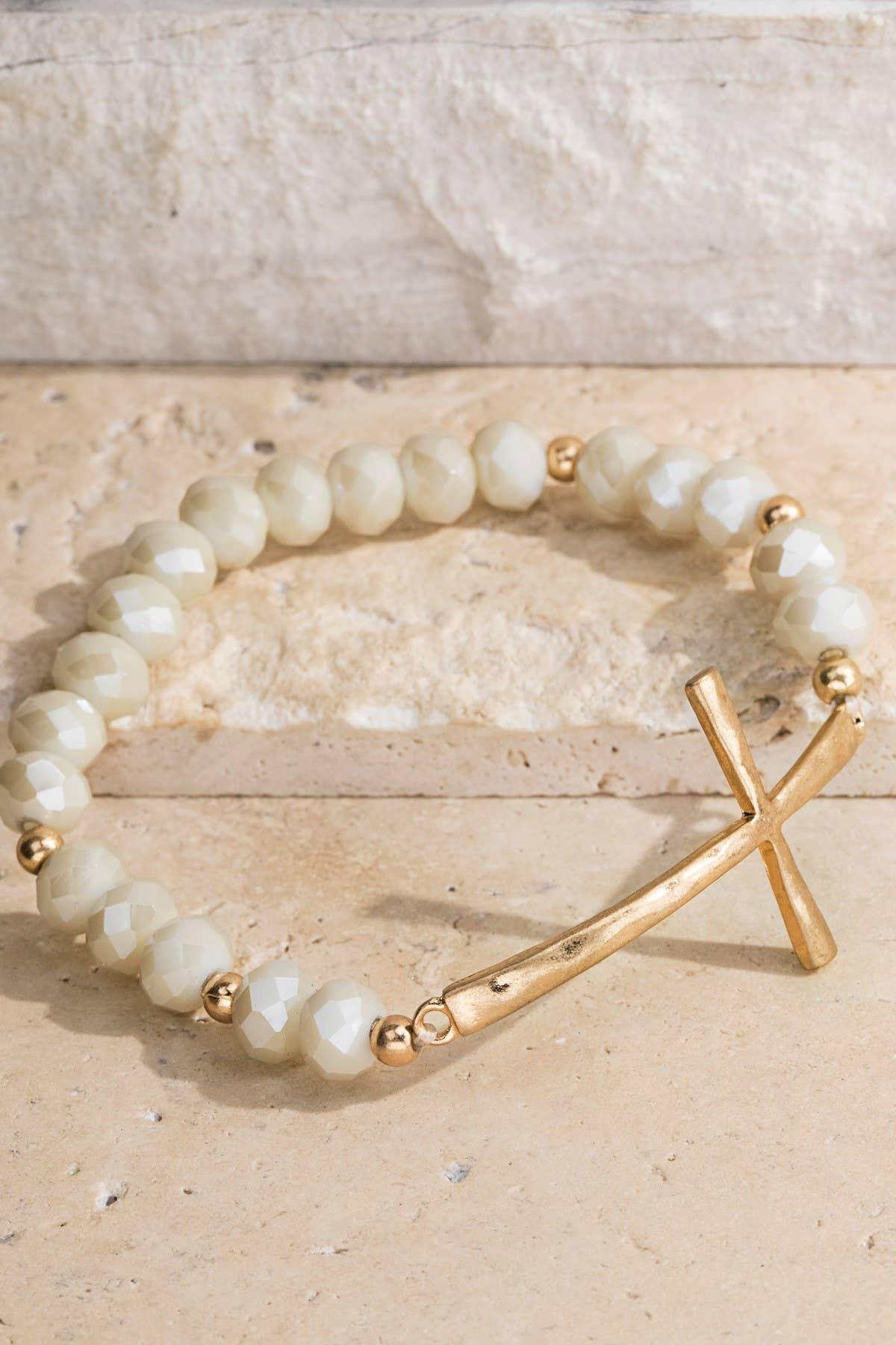 Faceted cream beaded bracelet with gold cross charm on stone background