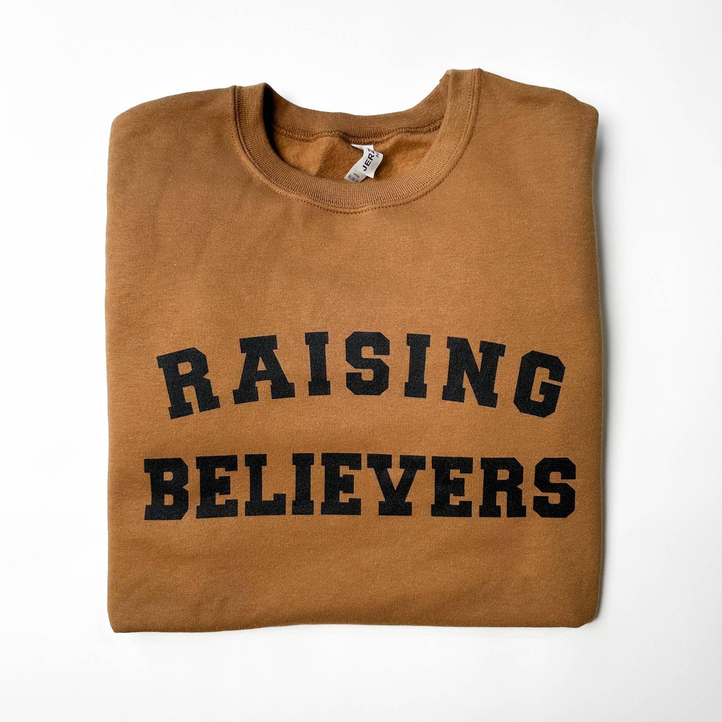 Folded brown crewneck sweatshirt with 'RAISING BELIEVERS' text in black on front