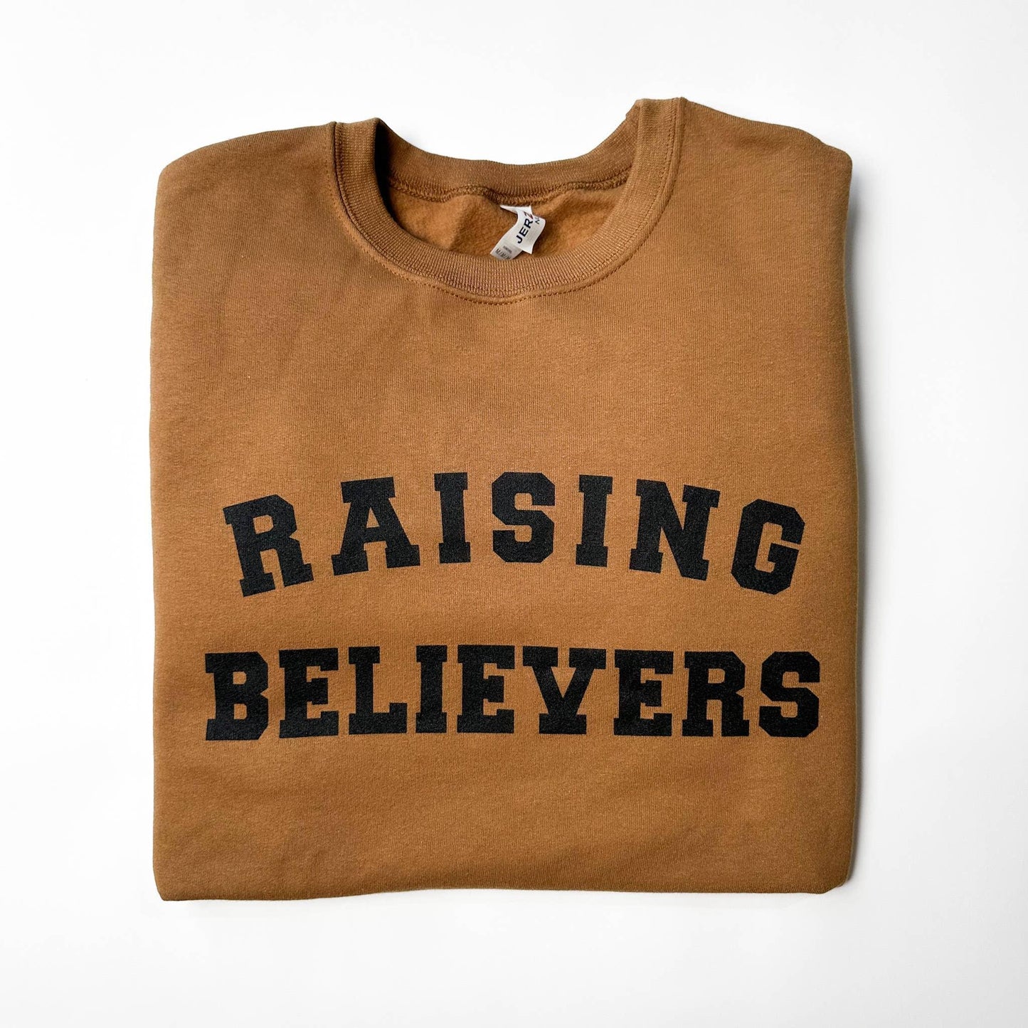 Folded brown crewneck sweatshirt with 'RAISING BELIEVERS' text in black on front