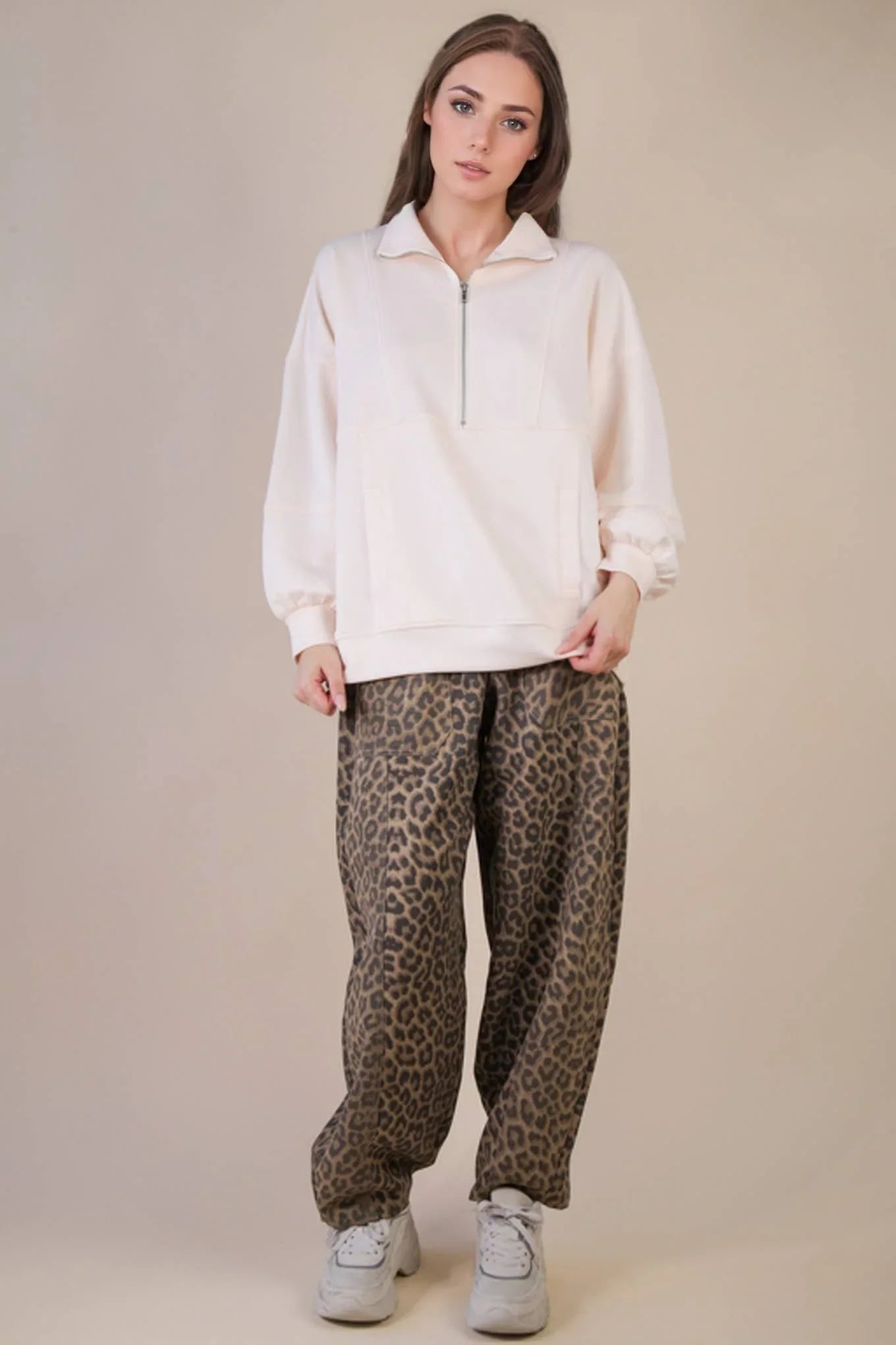Woman wearing a light pink quarter zip pullover with leopard print lounge pants and white sneakers