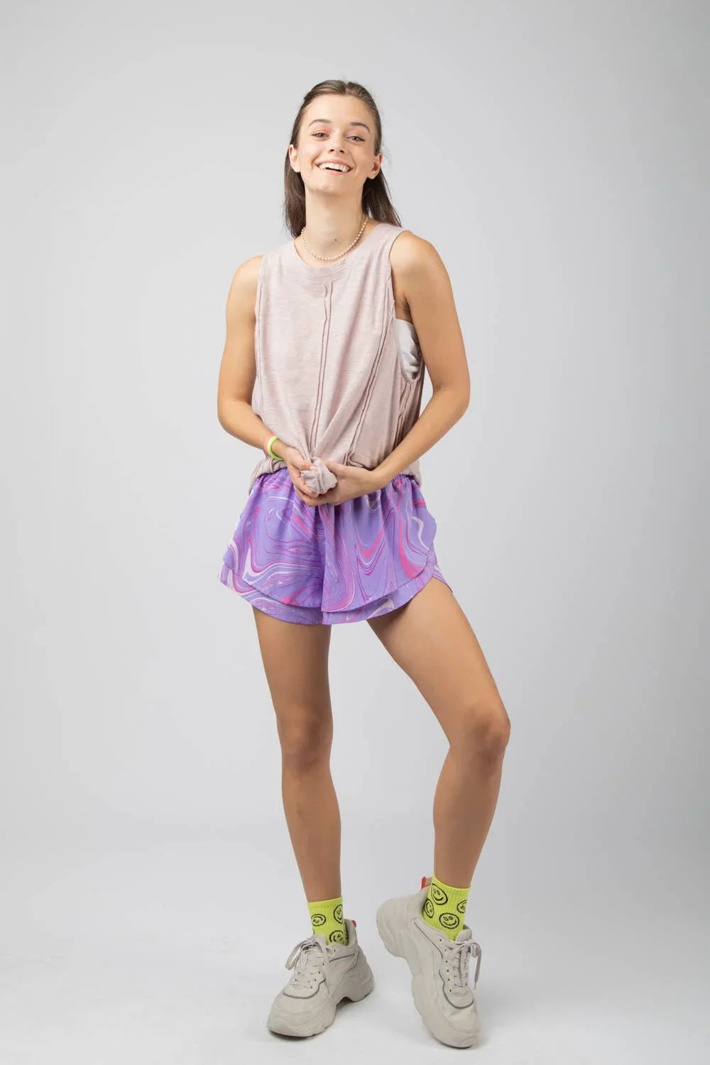 Woman in pastel sleeveless top and purple swirl shorts, neon smiley socks, chunky sneakers