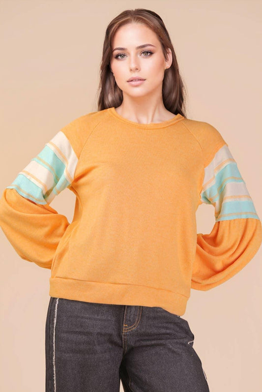 Woman wearing orange pullover with striped balloon sleeves and dark denim jeans