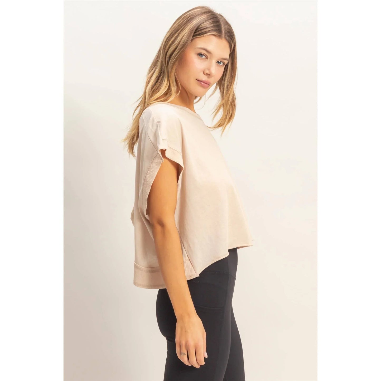 Woman wearing a loose beige short sleeve top with black leggings, side profile view