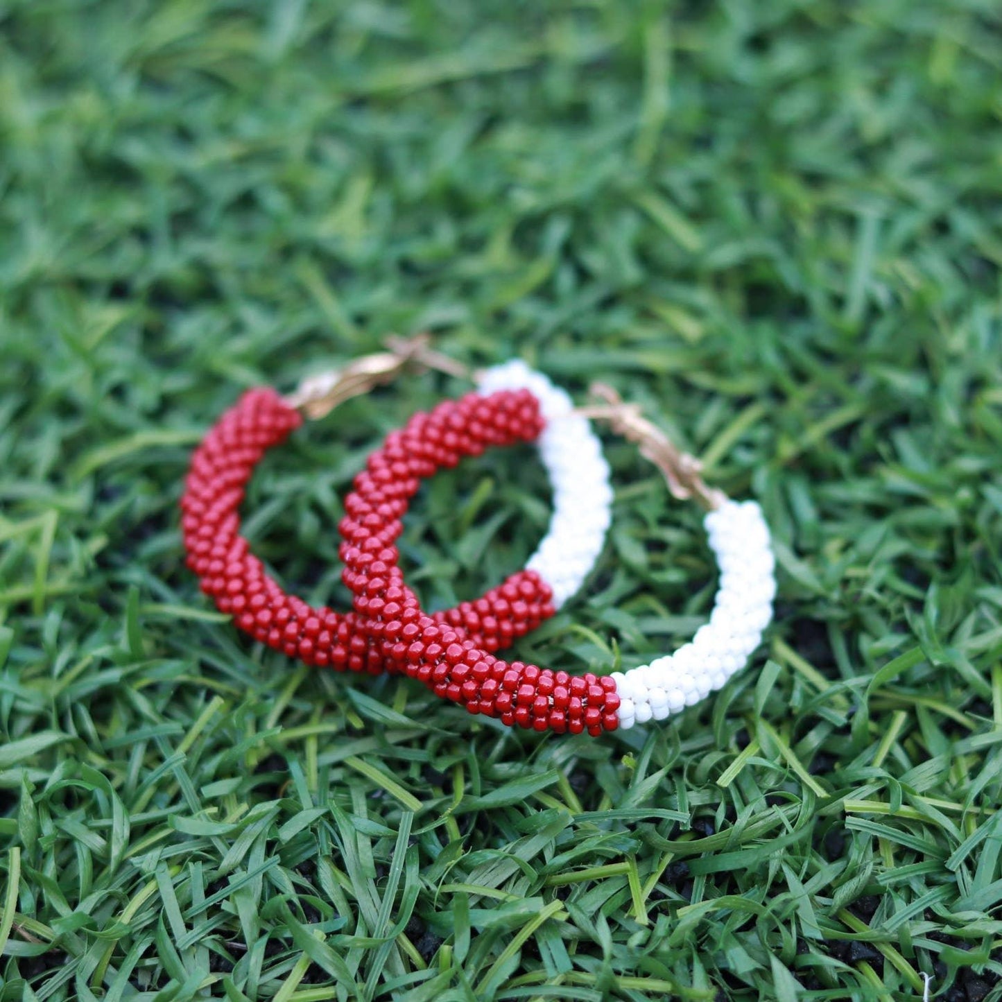 Red and white beaded hoop earrings on green grass background