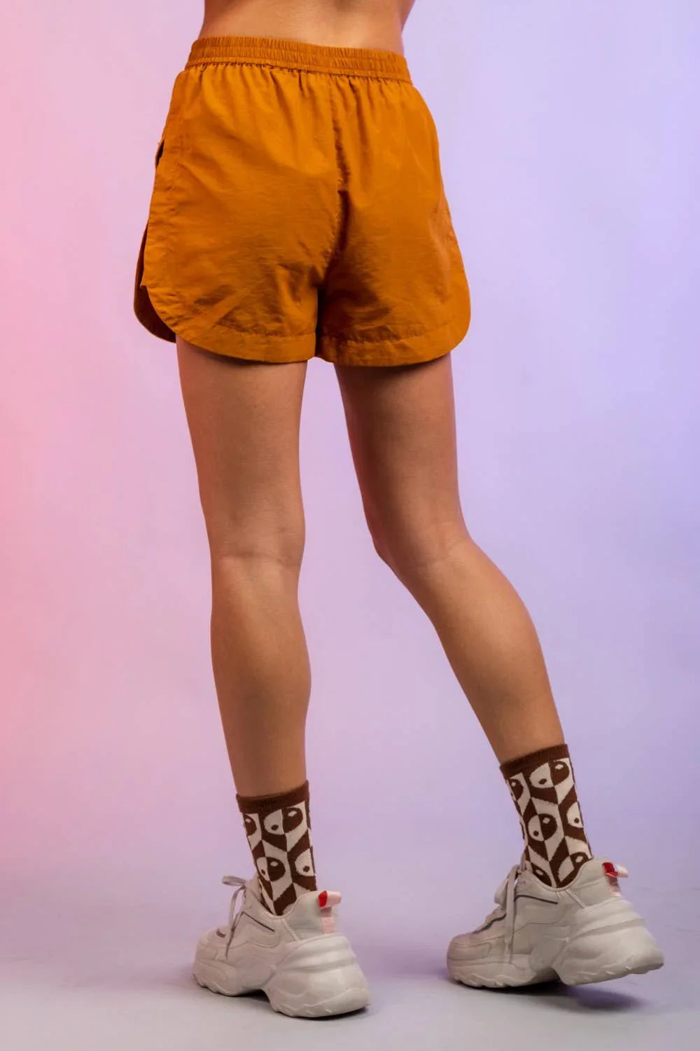 Back view of person wearing orange athletic shorts, patterned socks, and white sneakers