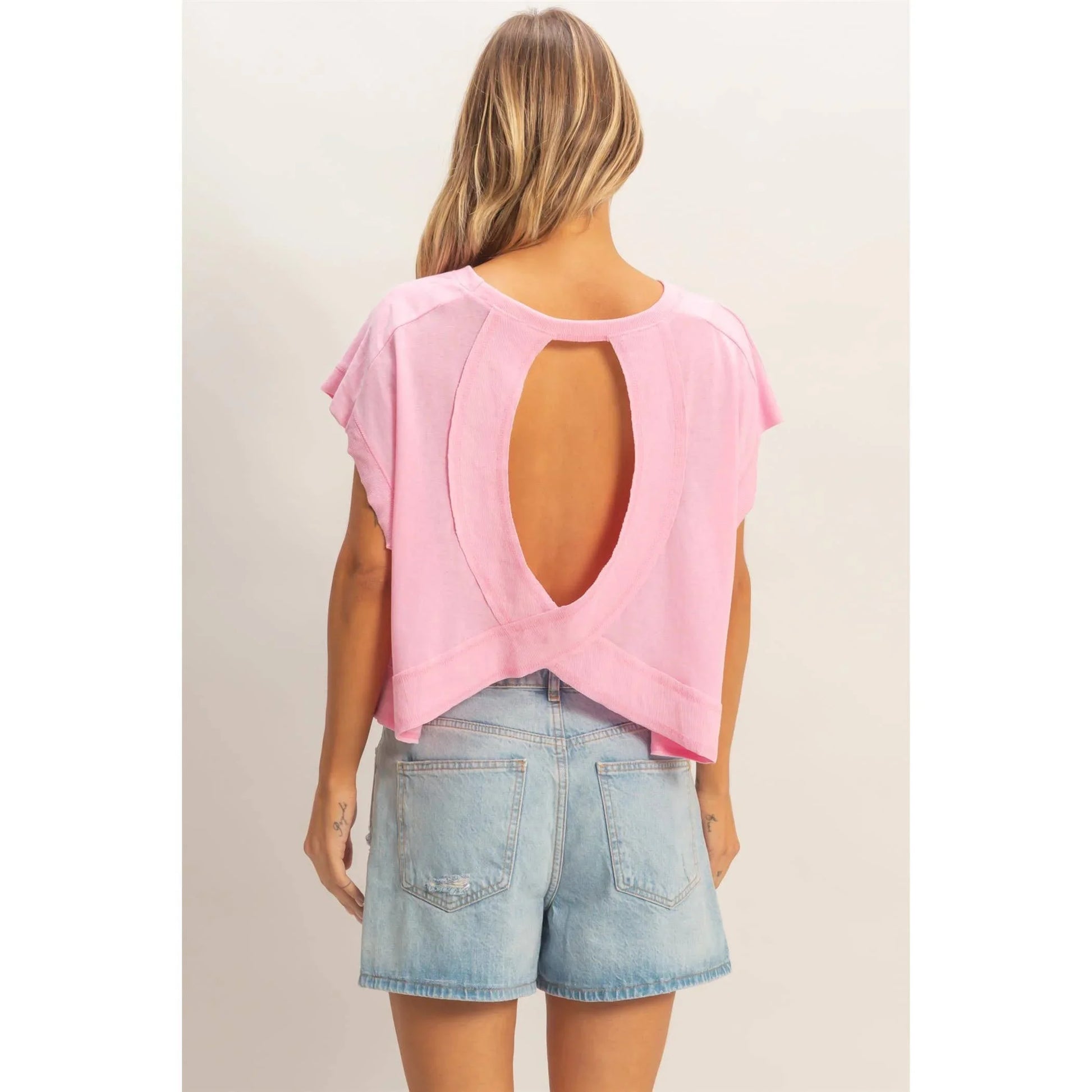 Woman in light denim shorts and pink open-back short sleeve top, casual summer style