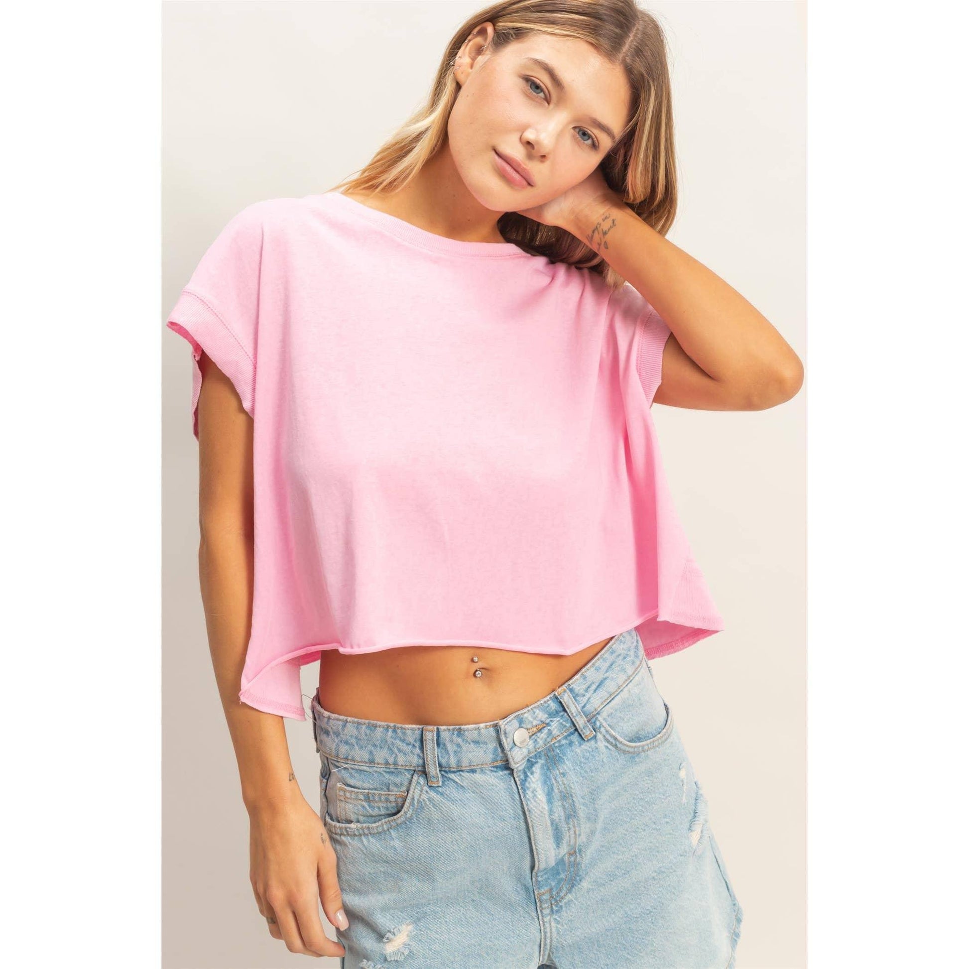 Woman in a pink cropped t-shirt and distressed denim shorts posing against a neutral background.