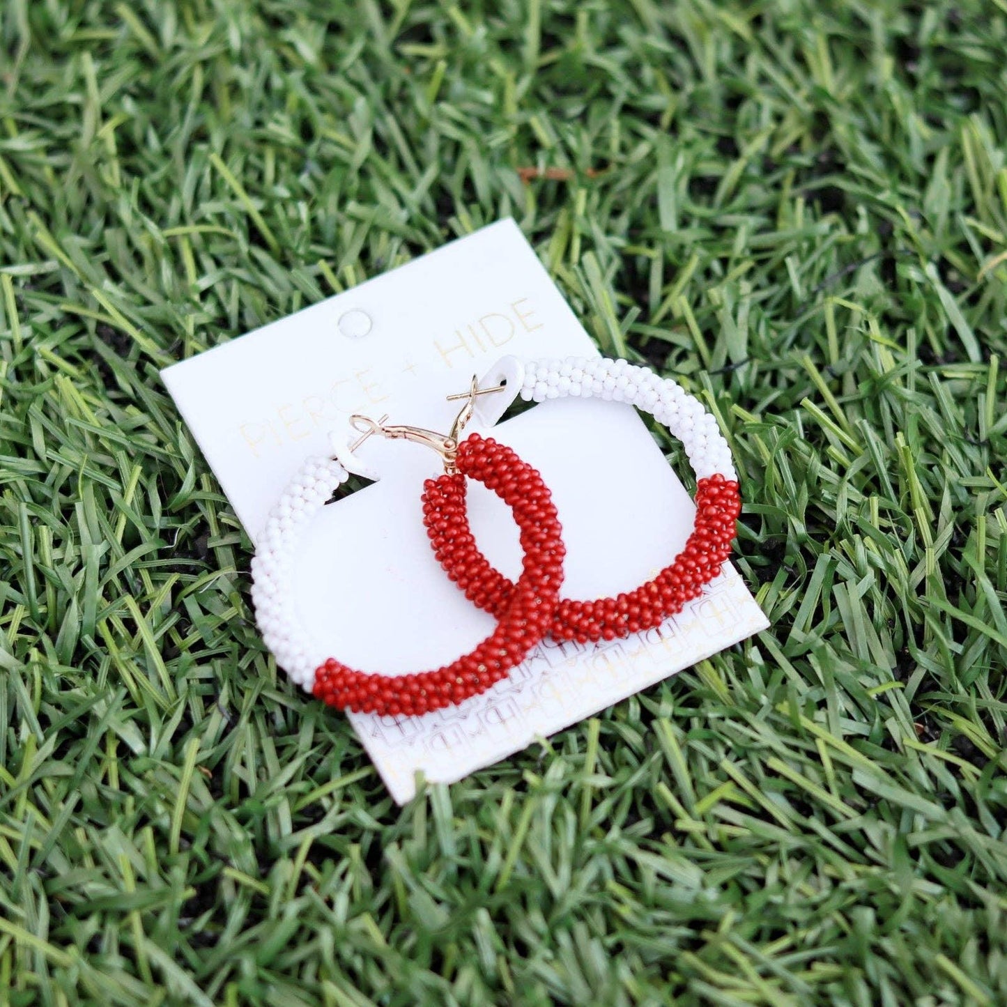 Red and white beaded hoop earrings on card display, laying on green grass