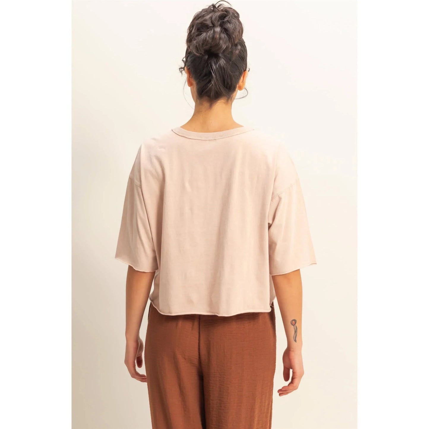 Back view of woman wearing blush cropped tee with short sleeves and brown wide-leg pants, minimalist fashion