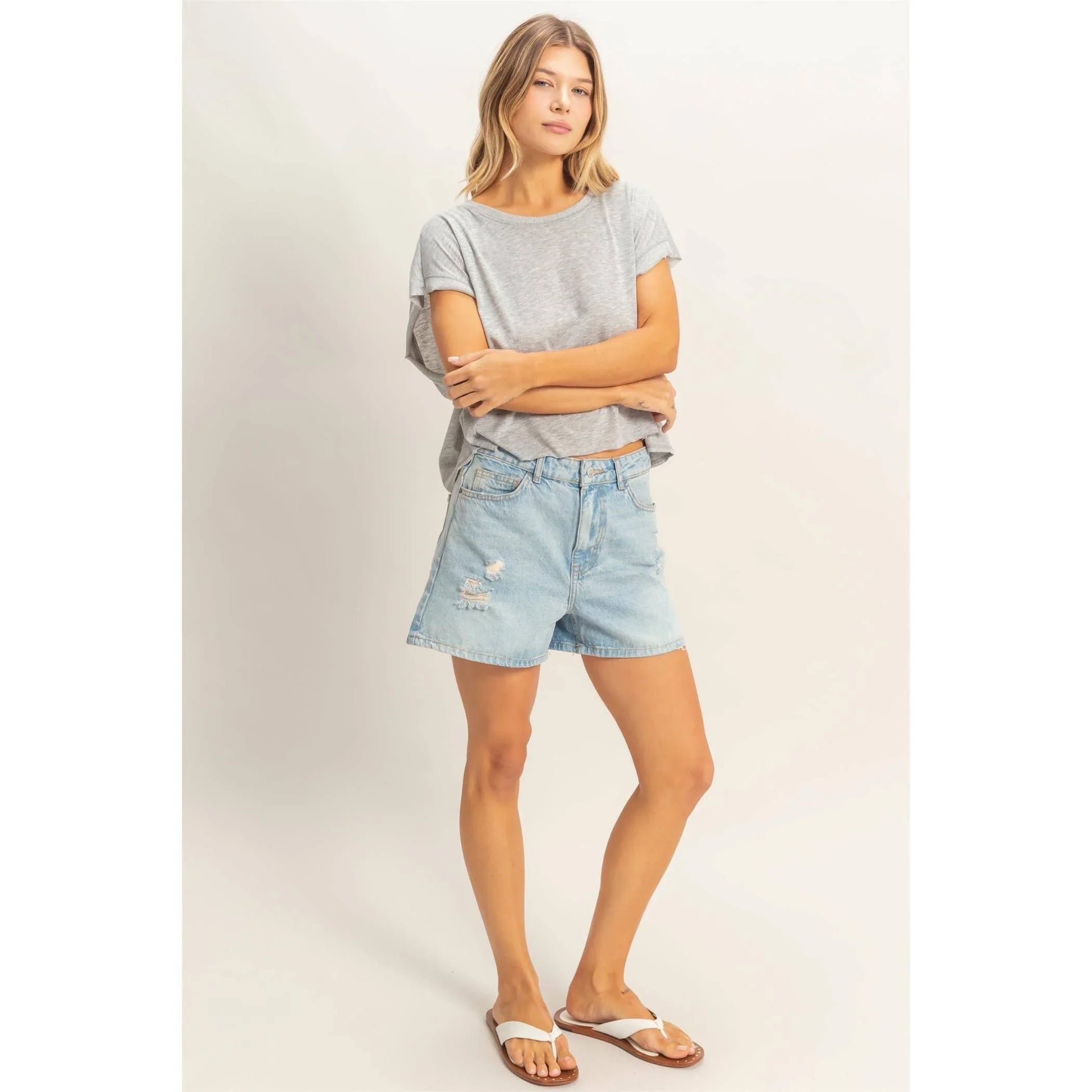 Woman wearing a grey t-shirt and light denim distressed shorts with white sandals