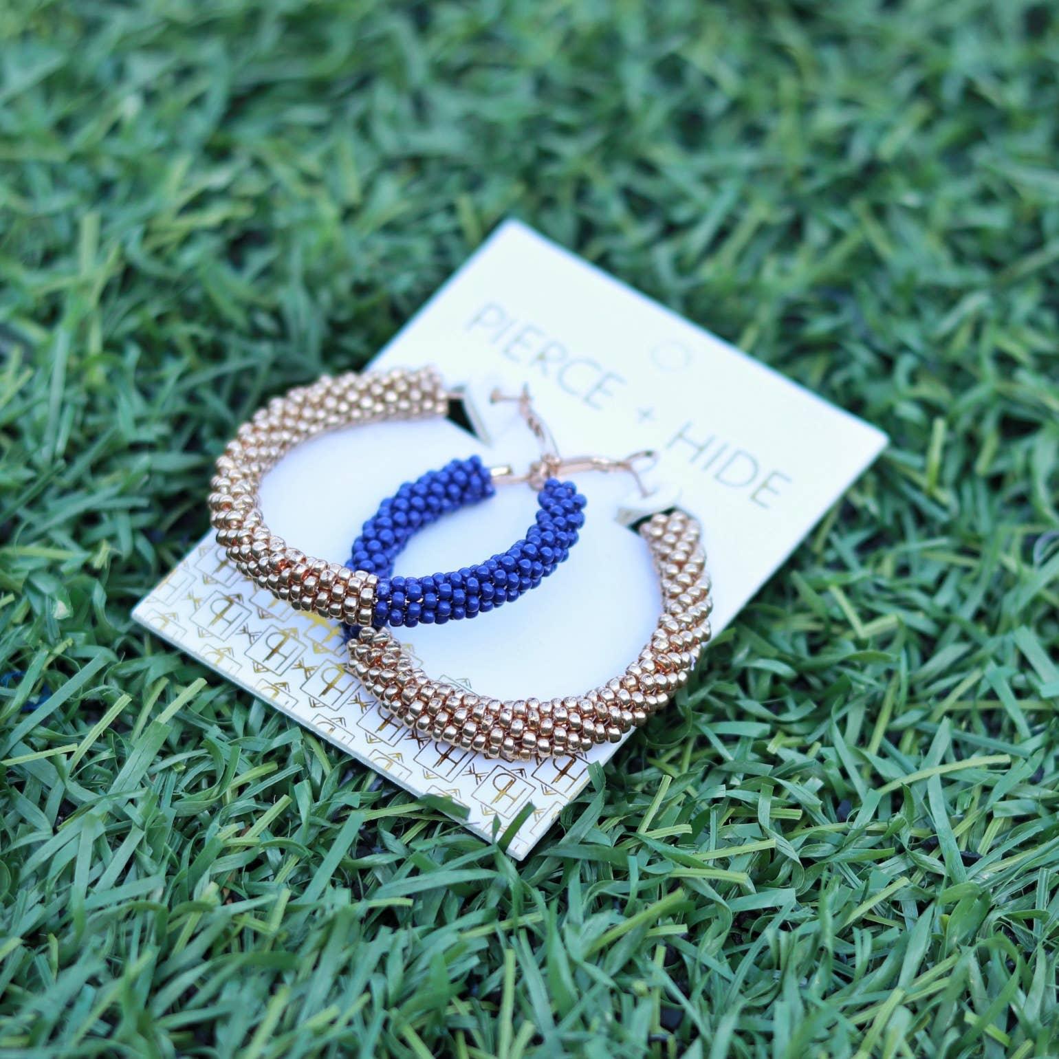 Gold and blue beaded hoop earrings on card displayed on grass