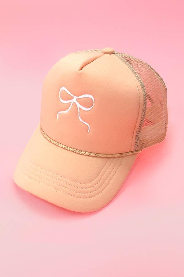 Peach mesh trucker hat with white embroidered bow on pink background