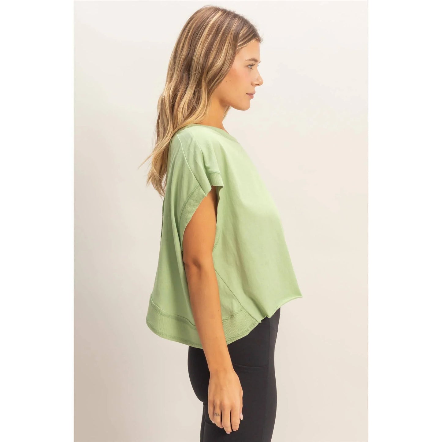Woman wearing loose sage green short sleeve top and black leggings, side view