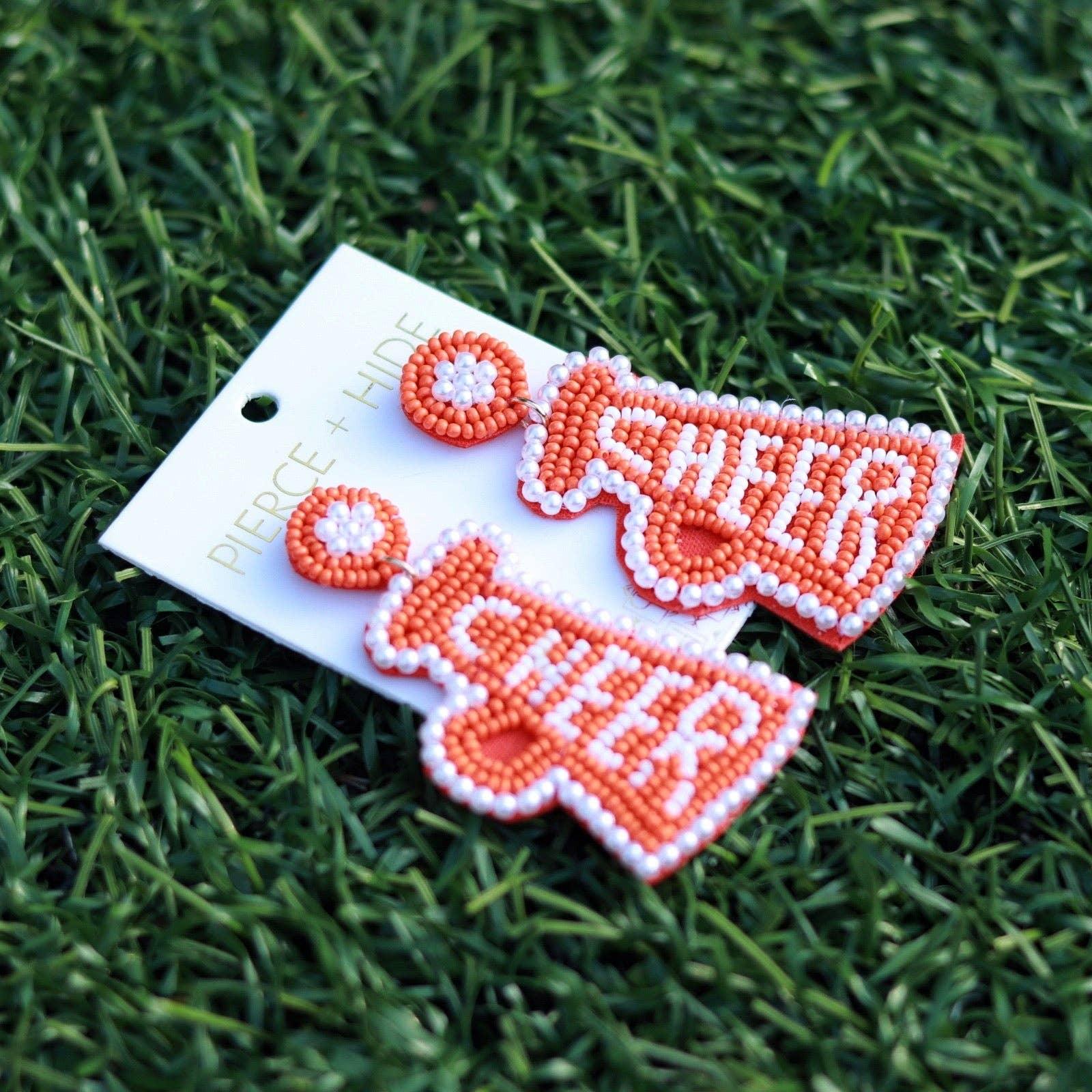 Beaded cheer megaphone earrings in orange and white on grass background