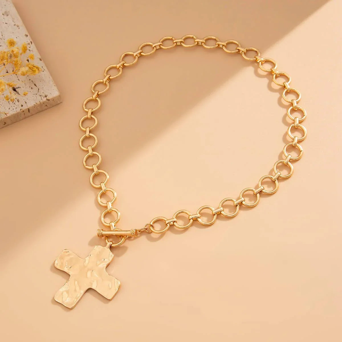 Gold chain necklace with hammered cross pendant on beige background