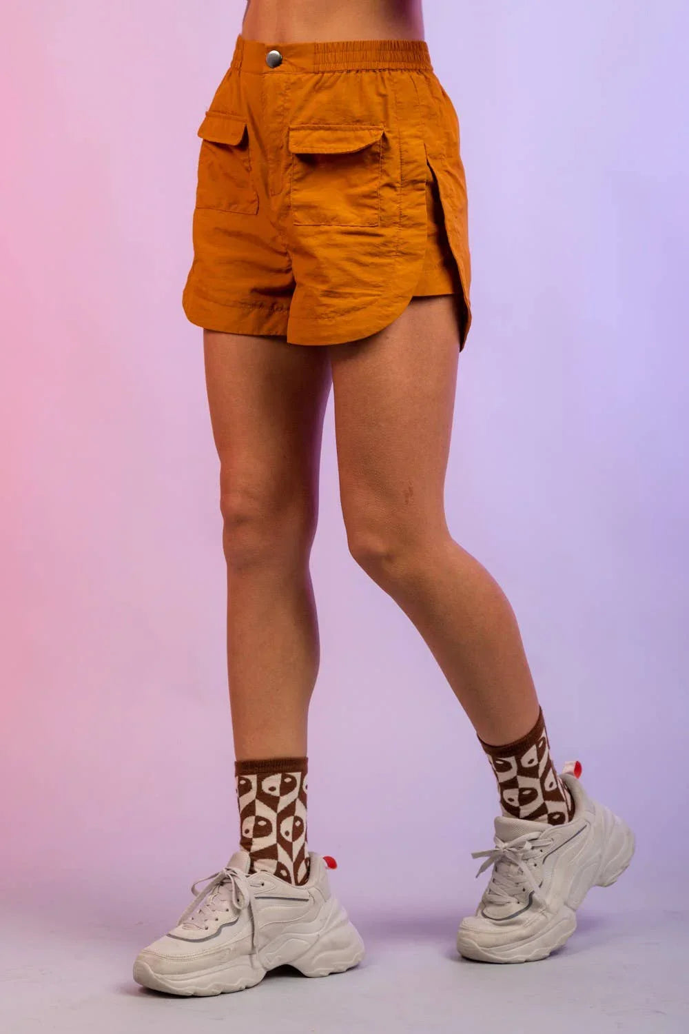 Woman wearing orange high-waisted shorts, graphic socks, and white chunky sneakers