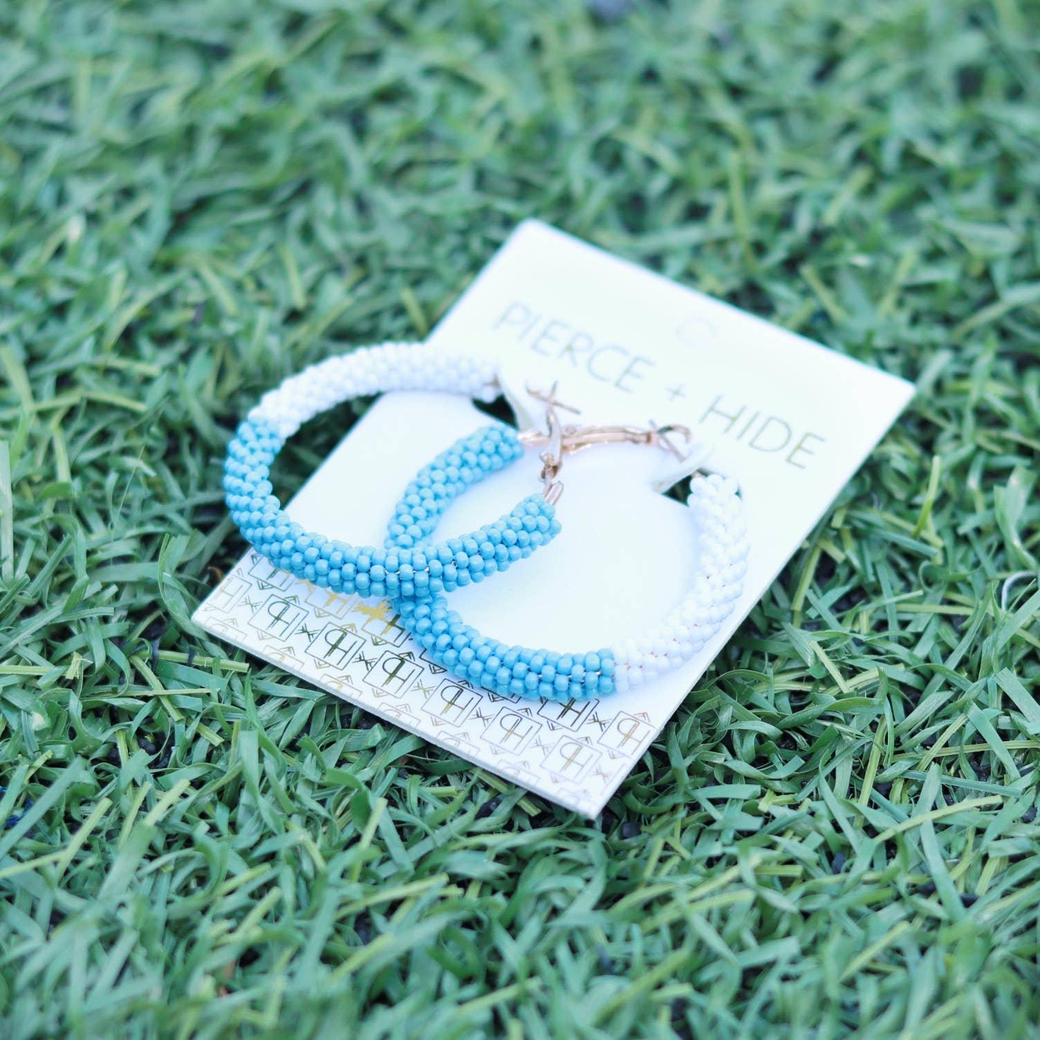 Blue and white beaded hoop earrings on card, displayed on green grass