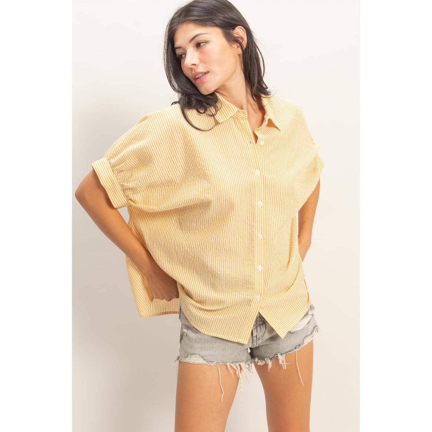 Woman wearing an oversized yellow striped button-up shirt and distressed denim shorts