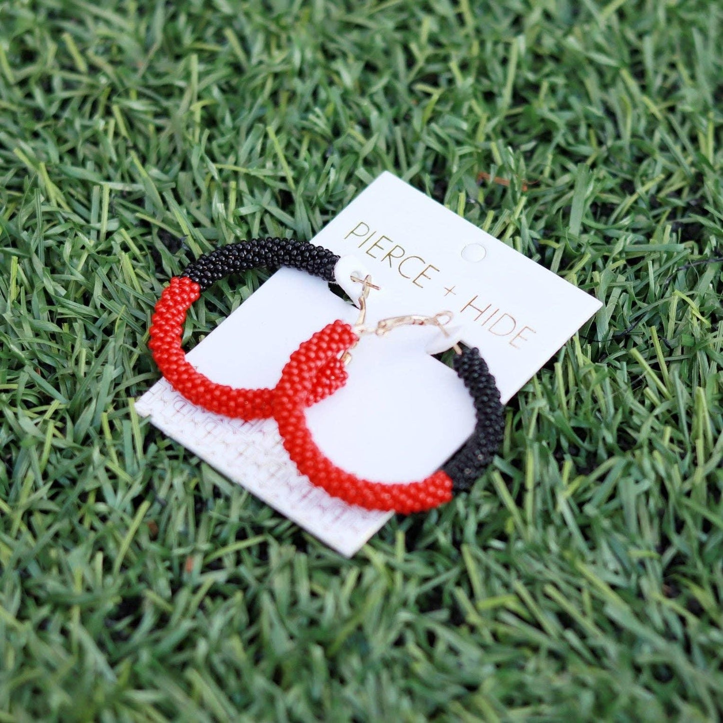 Red and black beaded hoop earrings with gold clasps on grass background