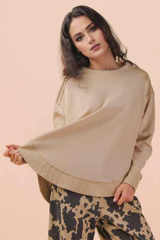 Woman wearing a beige oversized sweater and patterned wide-leg pants, neutral background