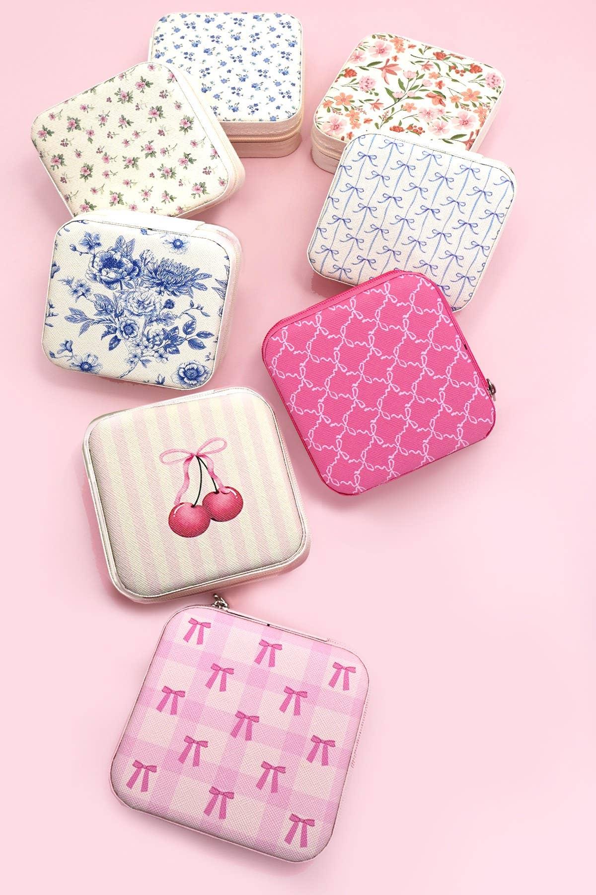 Assorted pastel square zipper pouches with floral, bow, and cherry patterns on a pink background.